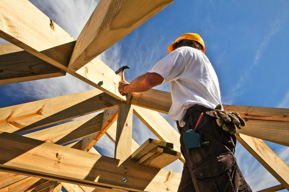 Charpentier en sécurité travaillant sur une charpente bois en construction extérieure, casque orange, assemblage de poutres et chevrons